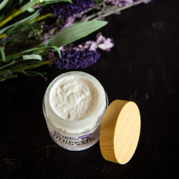 Jar of cream with a wooden lid on a dark background with lavender flowers