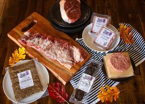 Assorted raw meats including ribs, steaks, and ground beef on a wooden cutting board with fall leaves.