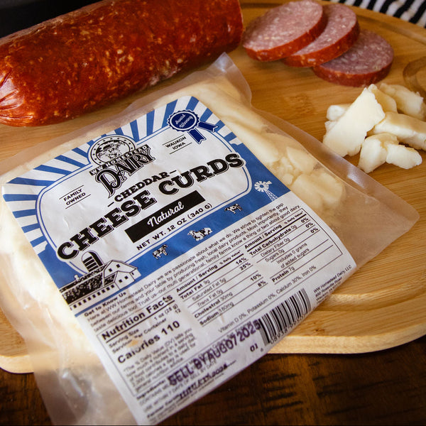 Packaged cheese curds with a salami and sliced meat on a wooden board.