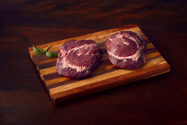 Two raw beef cheeks on a wooden cutting board.