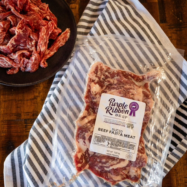 Packaged fajita  beef on a striped towel with a plate of raw beef in the background.