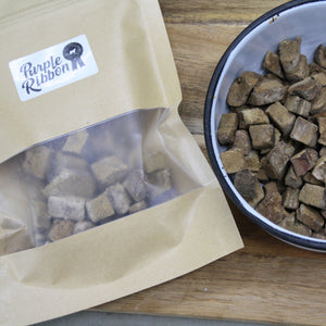 Dog treats in a bowl and packaging with 'Purple Ribbon' branding on a wooden surface.