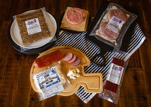 Assorted packaged meats and cheese on a wooden cutting board with striped cloth underneath.