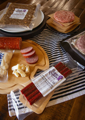 Assorted deli meats and cheeses on a wooden cutting board with striped towel underneath.